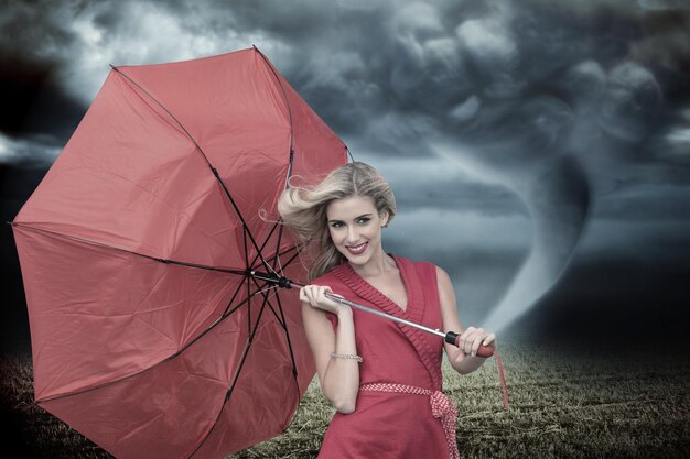 Foto bionda sorridente che tiene l'ombrello contro il cielo tempestoso con il tornado sul campo