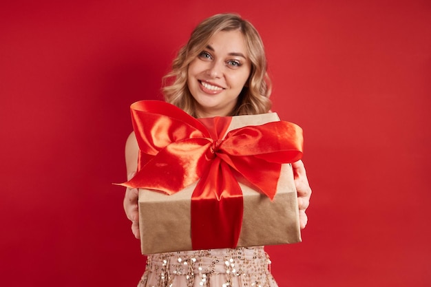 Smiling blonde holds out a box with a gift in front isolate on a red background selective focus