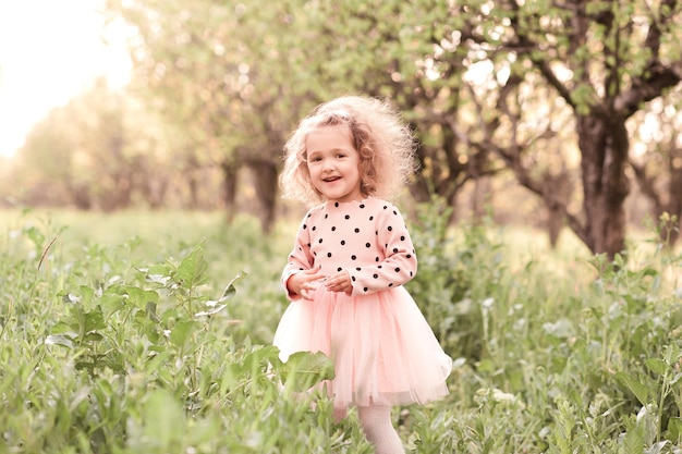 Smiling blonde kid girl walking in meadow in sunny day