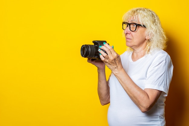 Smiling blonde old woman in white t-shirt holding a camera and looking to the side