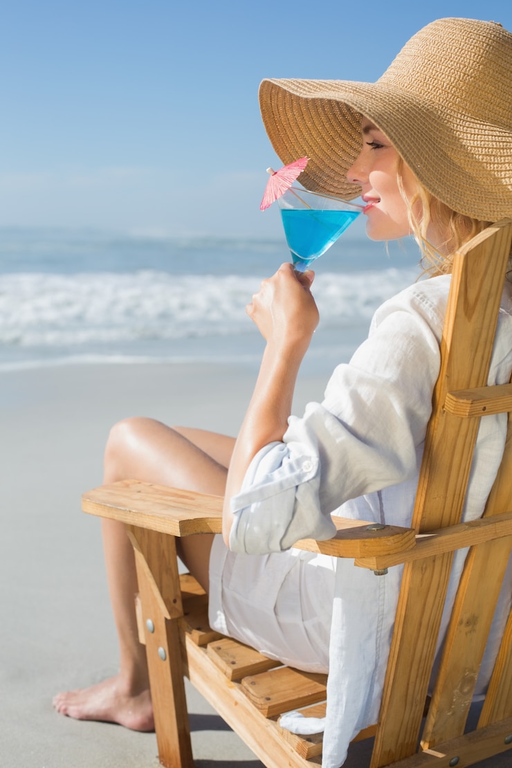 Photo smiling blonde relaxing in deck chair by the sea sipping cocktail