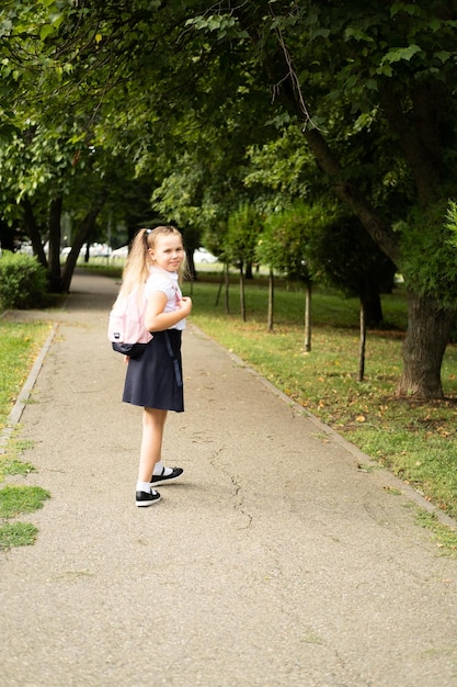 smiling blonde schoolgirl in school uniform with pink backpack going to school outdoor