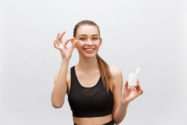 Smiling blonde sport woman holding bottle of medicine  