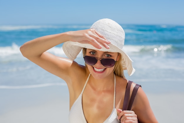 Bionda sorridente nella borsa di trasporto del bikini bianco sulla spiaggia