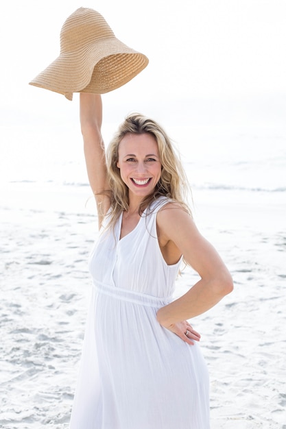 Smiling blonde in white dress looking at camera and holding straw hat