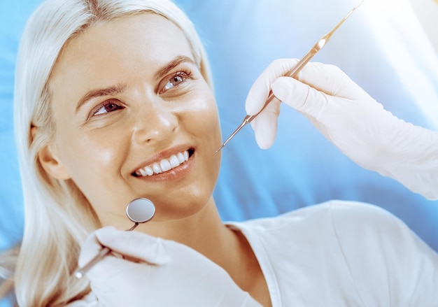 Donna bionda sorridente esaminata dal dentista presso la clinica dentale denti sani nel concetto di medicina