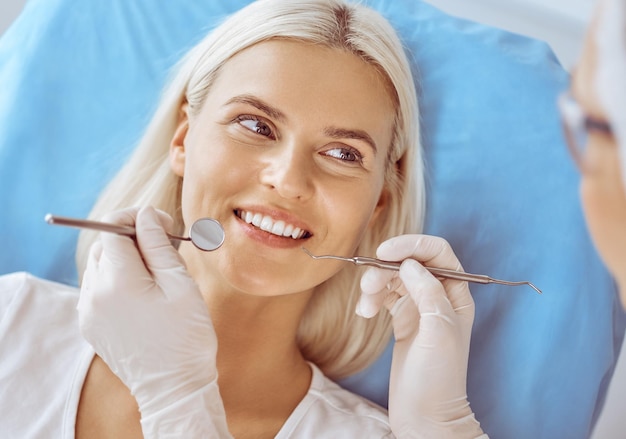 Smiling blonde woman examined by dentist at dental clinic. Healthy teeth and medicine concept.