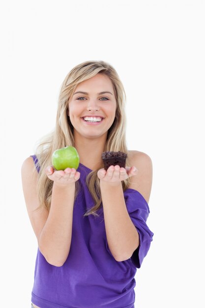 Photo smiling blonde woman hesitating between a muffin and an apple