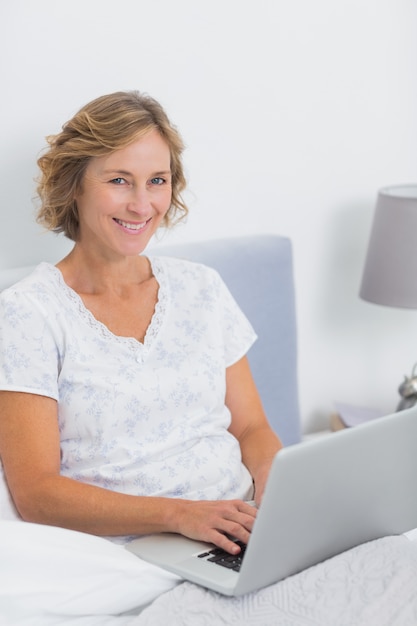 Smiling blonde woman sitting in bed using laptop 