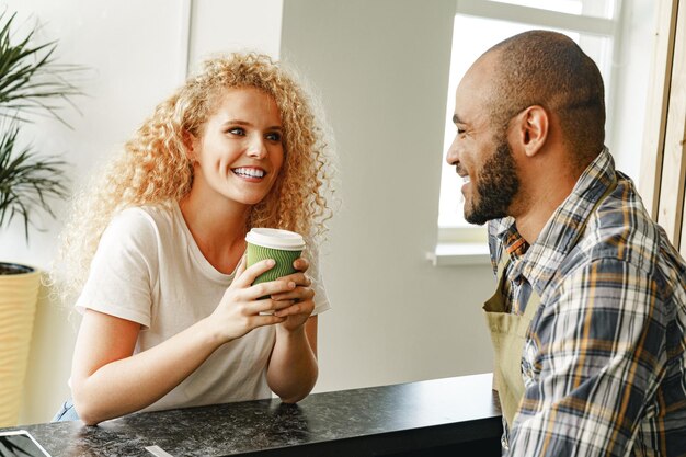 Photo smiling blonde woman talking to a waiter of a coffee shop at the counter