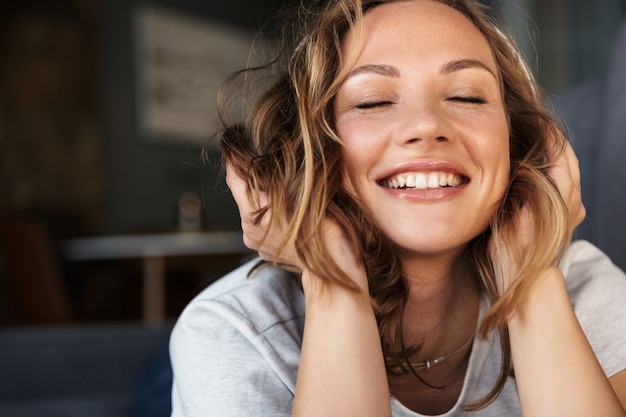 smiling blonde woman using wireless headphones while lying on sofa at living room