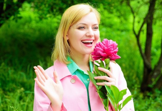 Smiling blonde woman with peony flower outdoors. Beautiful girl in garden.