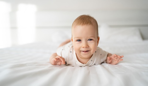 Smiling blueeyed baby girl four months old lying on the bed looking at the camera baby care toodler in the bedroom at home white background