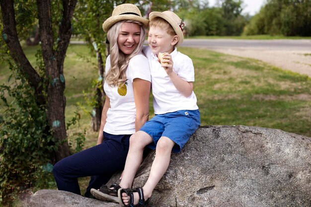 写真 笑顔の男の子と母親は木に寄りかかって岩の上に座っています