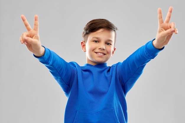 smiling boy in blue hoodie showing peace gesture