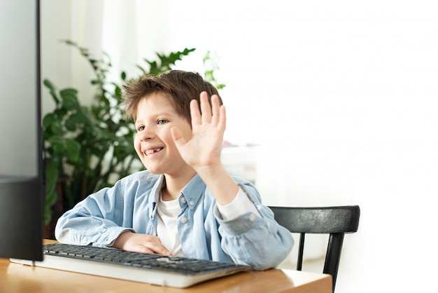 Smiling boy chatting online and waving at the computer screen. Kids and gadgets. Distance learning during isolation during quarantine. Boy and laptop at home. Lifestyle