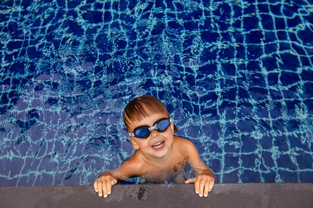 Smiling boy in goggles in water near edge of pool