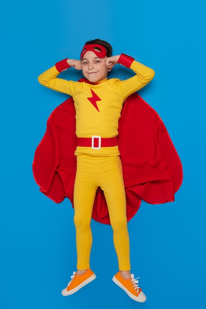 Smiling boy in hero costume lying on blue background