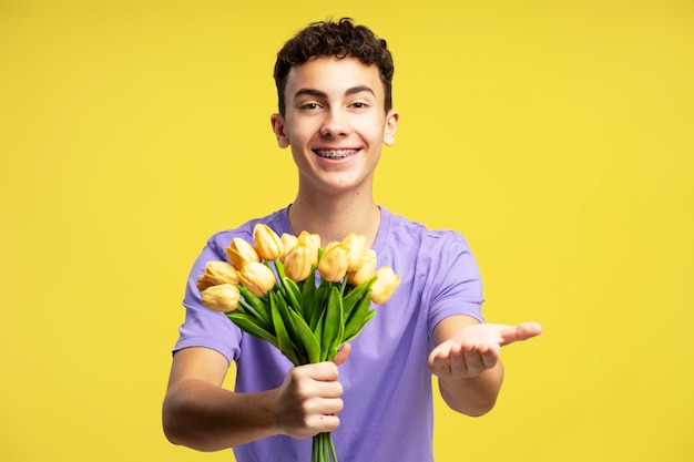 Smiling boy holding bouquet of spring tulips isolated on yellow background Holiday mothers day