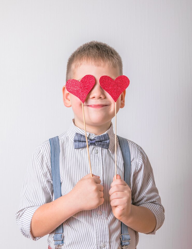 Smiling boy holding a red heart on eyes