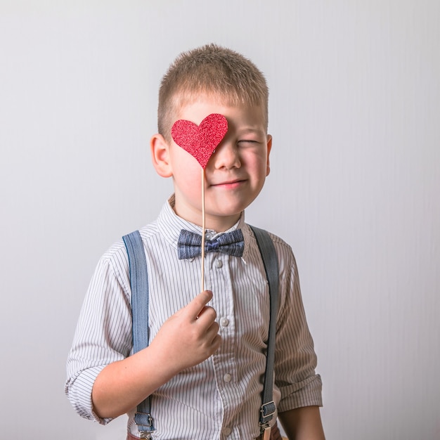 Ragazzo sorridente che tiene un cuore rosso sugli occhi