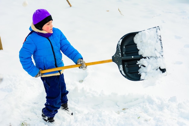 笑顔の男の子がシャベルで雪を運んでいる子供が降雪後に庭を掃除する