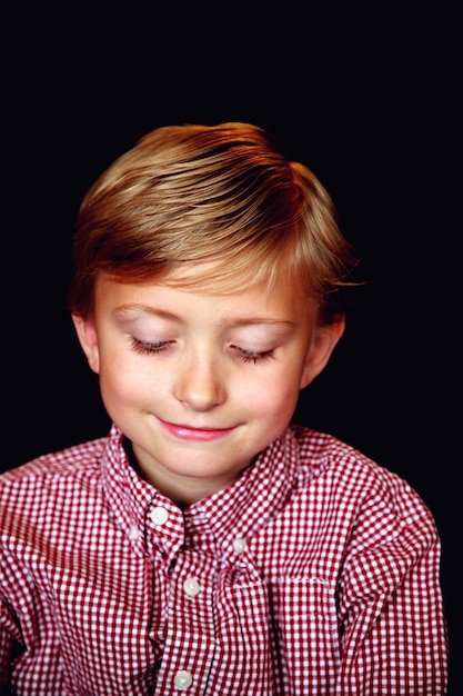 smiling boy looking down against black background