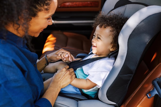 Photo smiling boy looking at mother tying seat belt