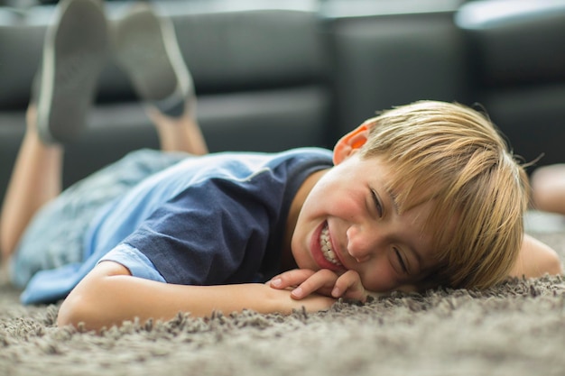 Photo smiling boy lying down on carpet at home