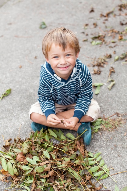 裏庭で落ちた乾いた葉で遊ぶ笑顔の少年