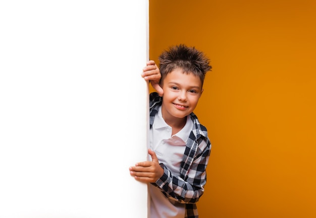 A smiling Boy poses with a white poster looking into the camera on a yellow background The student advertises your text Layout with space to copy