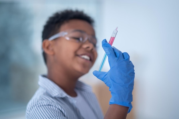 A smiling boy in protective eyeglasses holding a syringe in hand
