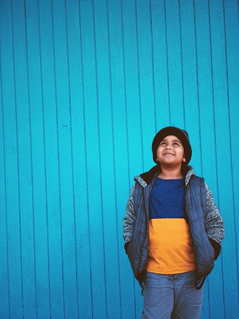 Foto ragazzo sorridente in piedi contro il muro blu