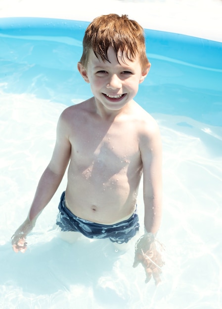 A smiling boy stands in a pool of blue water