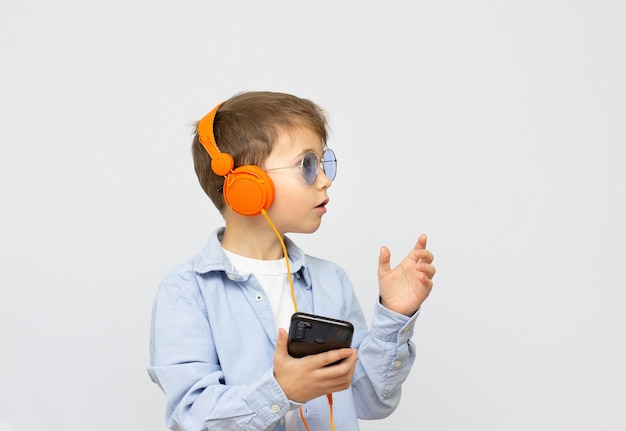 Smiling boy in sunglasses listening to music on headphones with phone