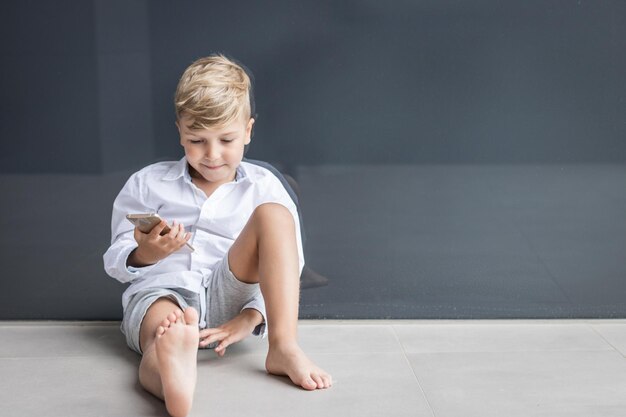 Photo smiling boy using mobile phone against wall