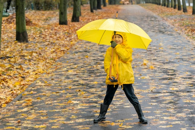 笑顔の少年が黄色い傘を持って公園を散歩する 雨の通りで子供と一緒に歩く