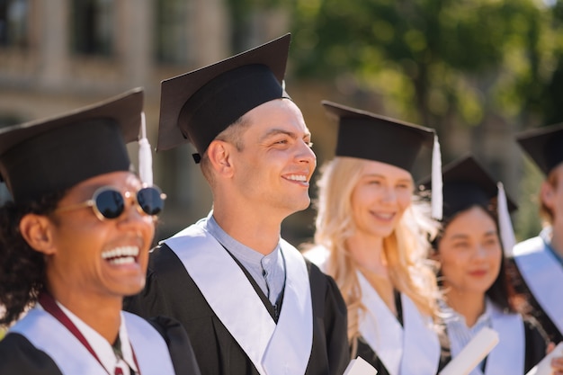 Smiling boy wearing masters cap standing among his friends during graduation ceremony