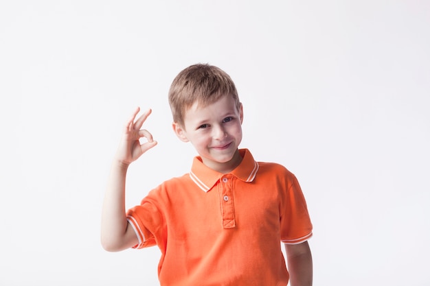 Photo smiling boy wearing orange t-shirt gesturing ok sign on white backdrop