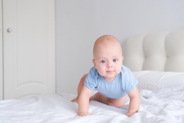 smiling boy with big blue eyes in a bodysuit learns to crawl on white bedding Healthy newborn baby