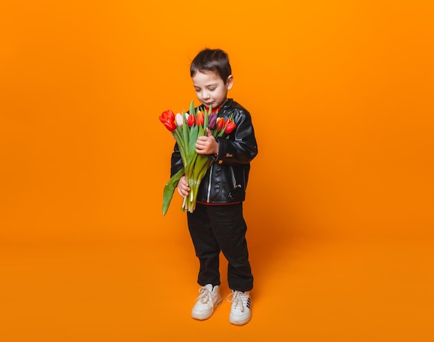 黄色に分離されたチューリップの春の花の花束と笑顔の少年チューリップを保持している小さな男の子