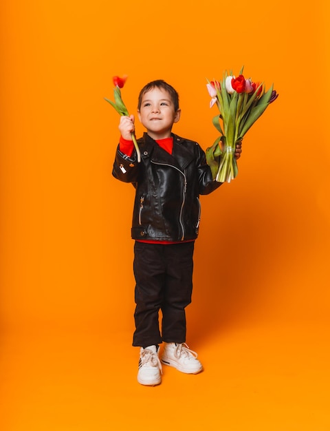 Smiling boy with spring flower bouquet of tulips isolated on yellow Little boy holding tulips