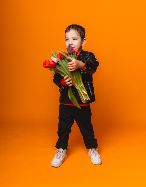 Smiling boy with spring flower bouquet of tulips isolated on yellow Little boy holding tulips