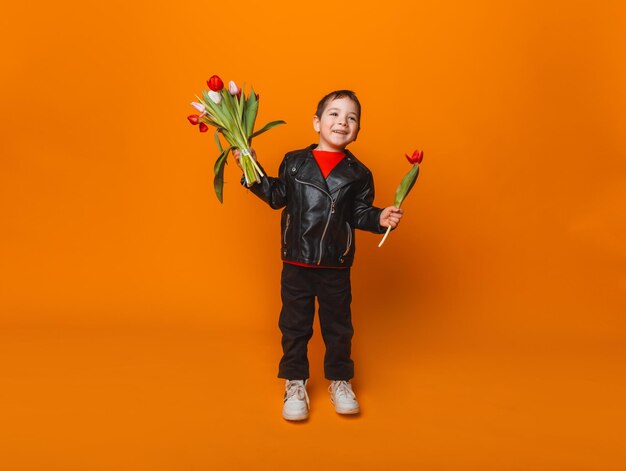 Smiling boy with spring flower bouquet of tulips isolated on yellow little boy holding tulips