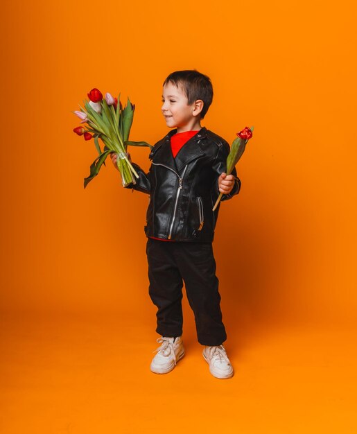 Smiling boy with spring flower bouquet of tulips isolated on yellow little boy holding tulips