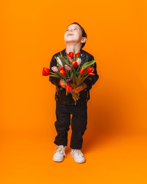 Smiling boy with spring flower bouquet of tulips isolated on yellow little boy holding tulips