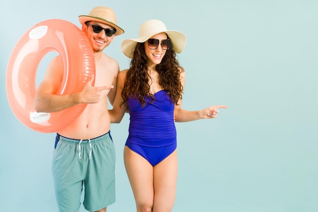 Улыбающиеся парень и девушка в купальниках, указывающие на копирайт на синем фоне. Красивая счастливая пара готова пойти в бассейн