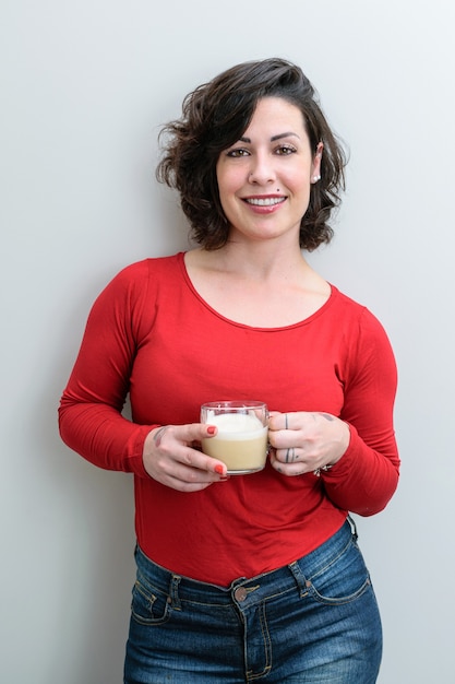 Smiling Brazilian woman facing the camera and holding a cup of cappuccino (vertical photo).