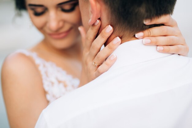 Smiling bride embraces the groom kissing her temple closeup