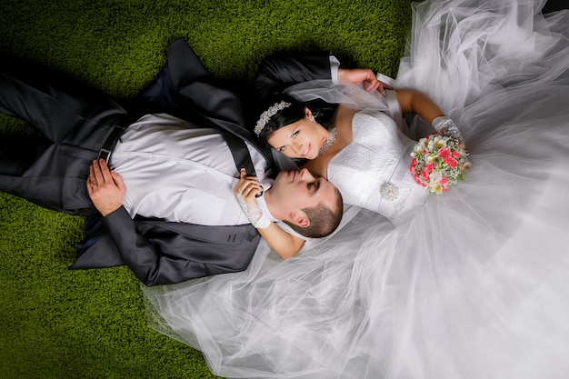 Smiling bride and groom lying on the grass-like carpet.